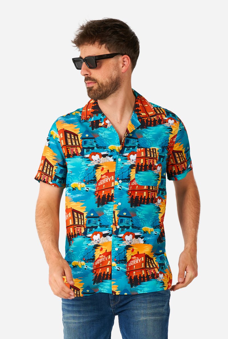 Camicia a maniche corte con bottoni, di colore blu brillante, con un motivo vivace di case e illustrazioni di personaggi in giallo, rosso e nero.