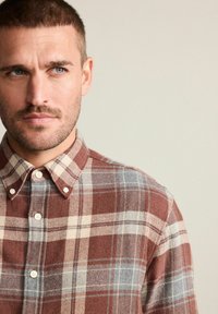 Camicia a quadri marrone e beige con accenti blu, dotata di colletto a bottoni. Realizzata in un tessuto testurizzato con una finitura morbida.