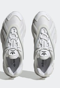 Vita träningsskor med mesh och syntetiskt övermaterial. Har snörning, cirkulära detaljer och tydlig Adidas-logotyp på tungan.