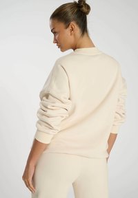 Beige Sweatshirt mit lässiger Passform, gerippten Bündchen und überschnittenen Schultern. Weicher Stoff mit glatter Textur und besticktem Detail am Ärmel.