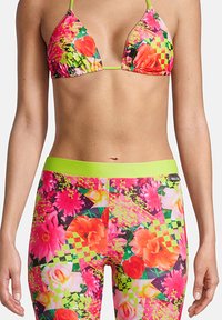 Haut de bikini avec des motifs floraux colorés en rose, orange et vert, associé à des leggings taille haute présentant le même design vibrant.