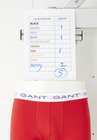 Red GANT boxer briefs on a mannequin below a paper listing color variations with handwritten amounts totaling five.