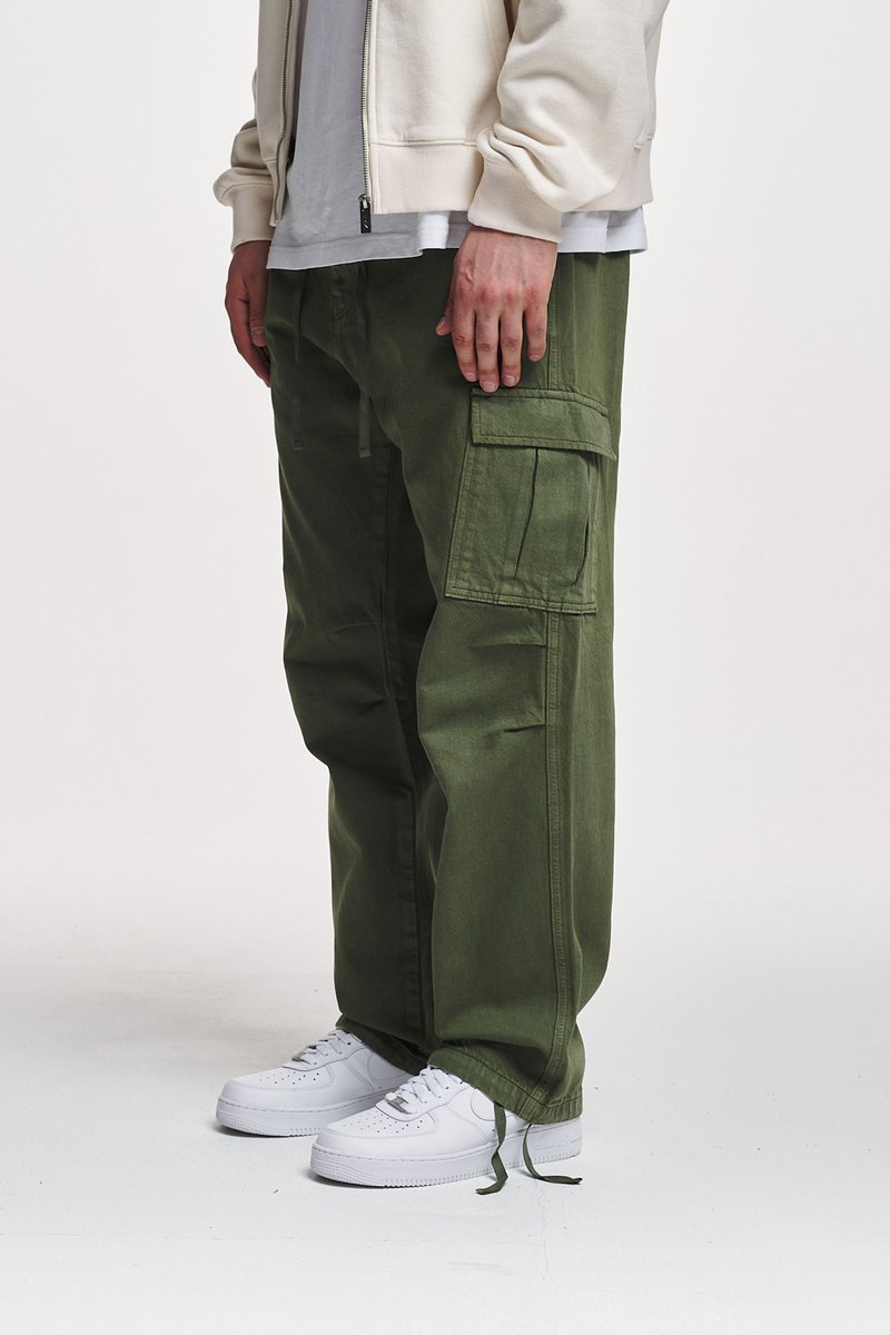 Pantalones cargo en algodón verde oliva con múltiples bolsillos, ajuste relajado y dobladillos con cordón, combinados con zapatillas blancas.