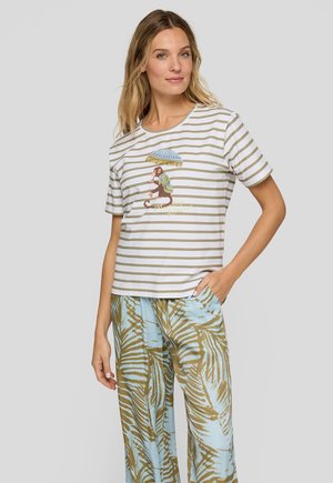 Frau trägt ein beige-weiß gestreiftes T-Shirt mit einem Affen, der einen Regenschirm hält, und blaue Hosen mit weitem Bein und braunen Blattmustern.