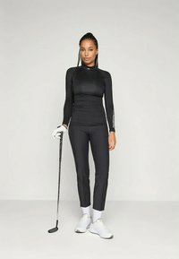 Čierne tričko s dlhým rukávom a priliehavé nohavice vyrobené z elastického materiálu; biele logo na rukáve; spojené s bielymi golfovými topánkami a rukavicou.