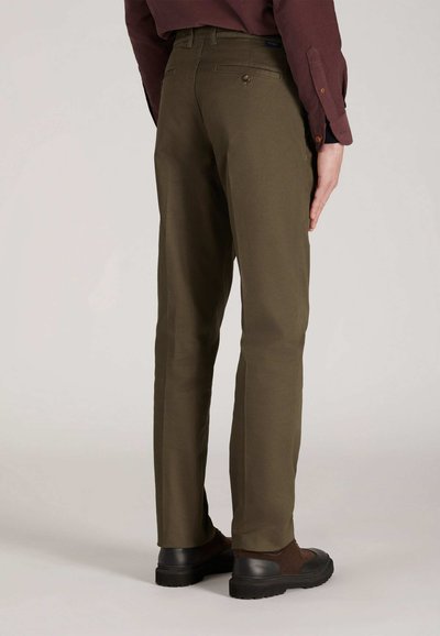 Olijfgroene broeken met een rechte snit, voorzien van een middelhoge taille, twee achterzakken en bruine schoenen met zwarte zolen.