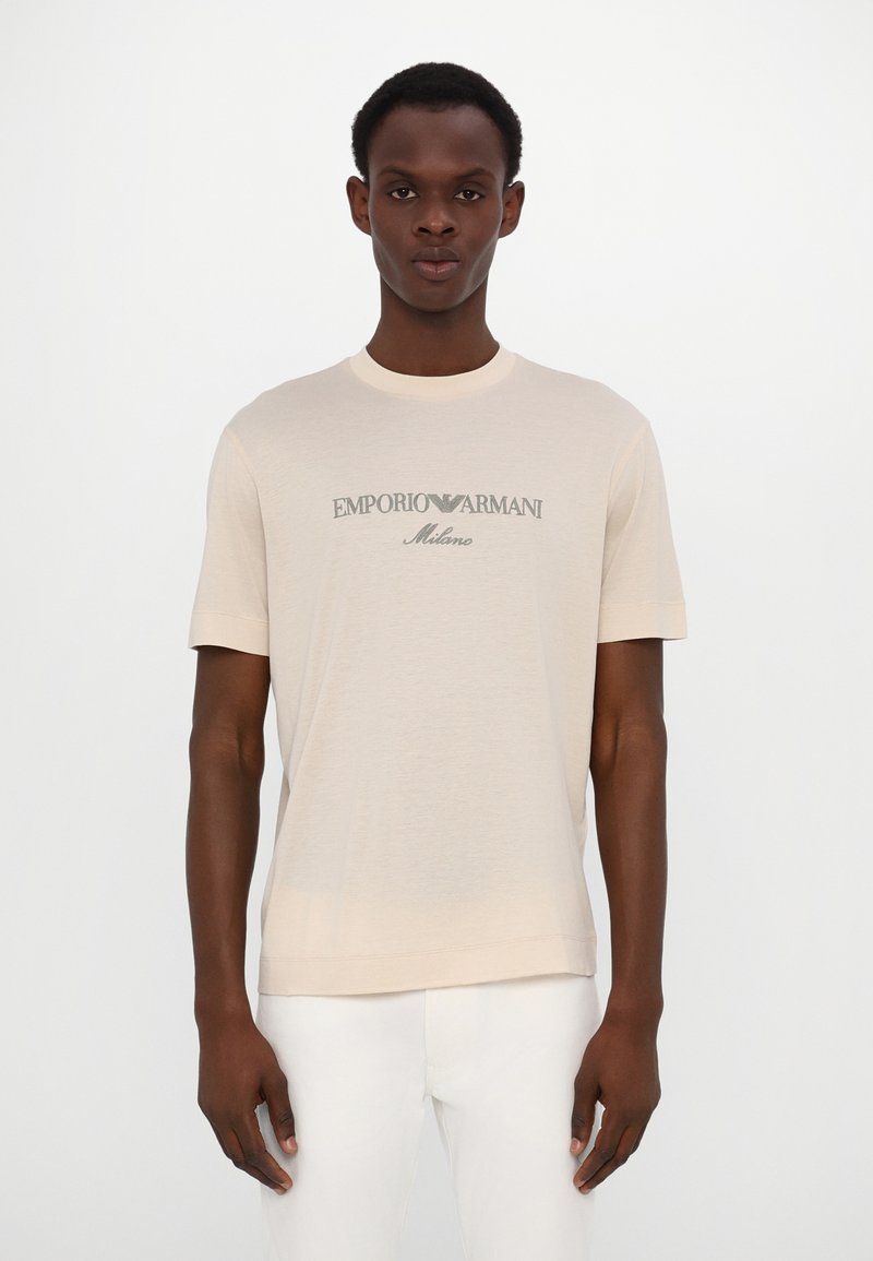 Bežinė trumpų rankovių marškinėlių su minkšta medžiaga, apvaliu iškirpimu ir tamsiai žalia „Emporio Armani Milano“ logotipu. Paprastas dizainas.