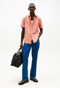 Camisa de manga corta a rayas rojas y blancas, combinada con unos vaqueros anchos azules. Un bolso de cuero negro y unos zapatos negros brillantes completan el conjunto.