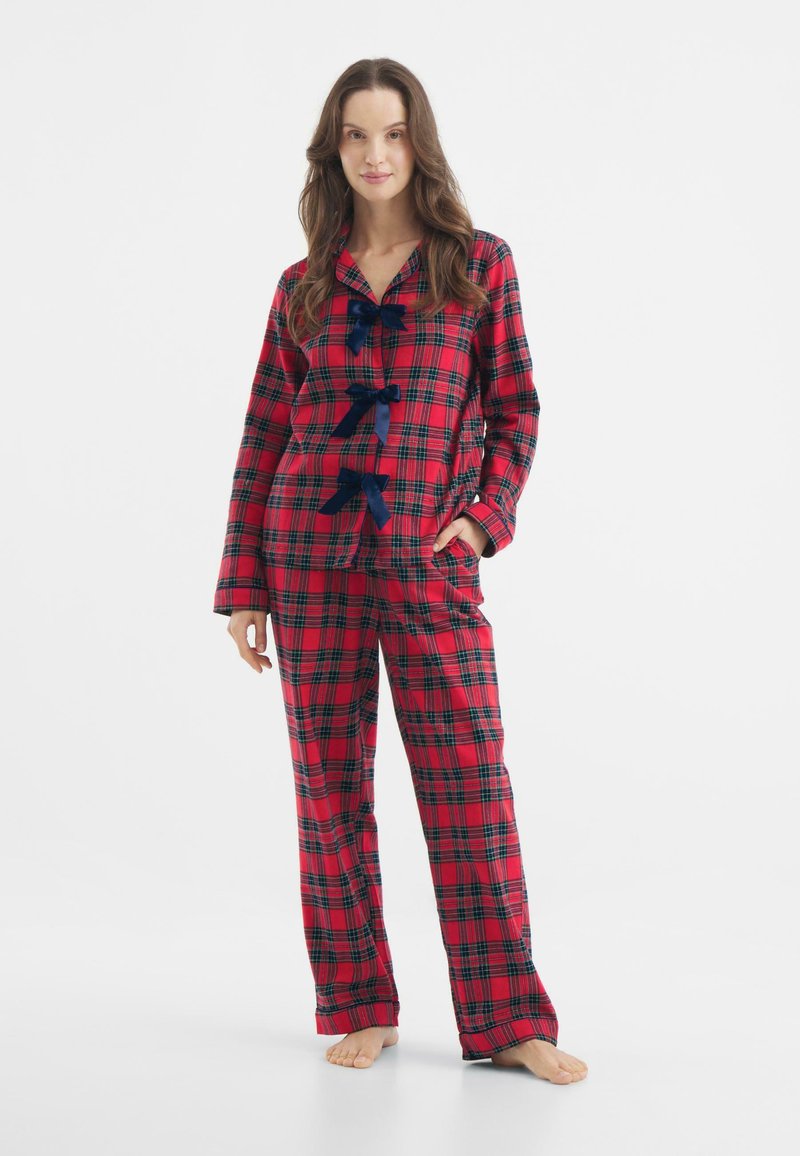 Conjunto de pijama a cuadros rojos y negros con parte superior de botones y pantalones a juego. Presenta detalles de cinta azul en el frente y una textura de tela suave.