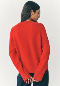 Maglione rosso a maglia con scollatura rotonda, polsini e orlo a coste. Presenta una vestibilità morbida e maniche lunghe. Colore semplice e uniforme, senza motivi.