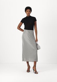 Black fitted top with a high neck, paired with a silver, glittery, maxi skirt, worn with strappy black heels and a small gray handbag.