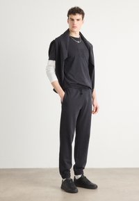Dark navy sweatpants and t-shirt outfit, featuring an embroidered logo, with a matching sweater draped over the shoulders, paired with black sneakers.
