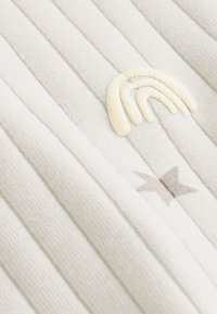 Close-up of white ribbed fabric with an embroidered cream semicircle and a gray star detail.