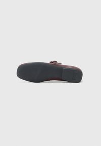 Burgundy leather shoe with a smooth surface and a textured black rubber sole. Features a low heel and rounded toe design.