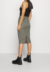 Svart tanktopp, knälång pennkjol i hundtandsmönster med slits bak, matchad med svarta läder Chelsea-boots med gula detaljer.