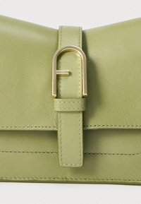 Πράσινη δερμάτινη τσάντα με λεία υφή, που διαθέτει χρυσό μεταλλικό κρίκο και λουρί λεπτομέρειες. Μινιμαλιστικός σχεδιασμός με διακριτική ραφή.