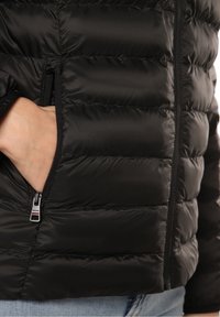 Czarna kurtka puchowa o pikowanej fakturze, z zamkniętą kieszenią po boku i elastycznymi mankietami. Gładki, błyszczący materiał o eleganckim designie.