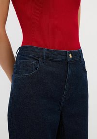 Tmavě modré denimové džíny s hladkou texturou, s přední kapsou, poutky na pásek a zlatým knoflíkem v pase.