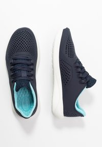 Chaussures de sport bleu marine avec une tige perforée, une doublure intérieure bleu clair et une semelle en caoutchouc blanche. Comprend une fermeture à lacets et un design respirant.