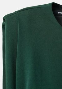 Zelený v-krkový top s měkkou, strukturovanou tkaninou, volným střihem a čistými liniemi. Výstřih a rukávy mají jednoduchý design.