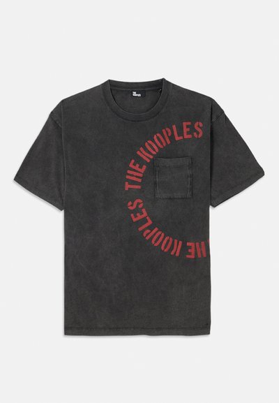 T-shirt de algodão preta com um gráfico redondo em texto vermelho a dizer "THE KOOPLES", apresentando um bolso frontal e um ajuste descontraído.