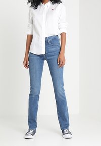 Ljusblå denimjeans med rak passform, hög midja och synliga sömmar. Matchas med en vit skjorta med knappar och blå sneakers.