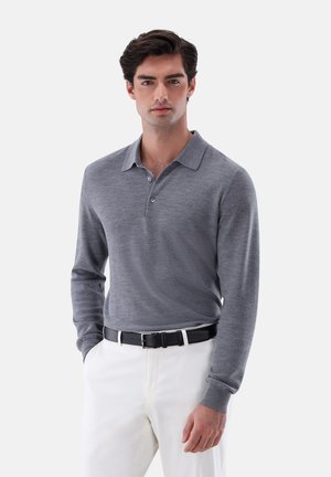 Graues Langarm-Polohemd mit Kragen, ausgestattet mit einer Knopfleiste. Kombiniert mit weißen Hosen und einem schwarzen Gürtel. Glatte Textur.