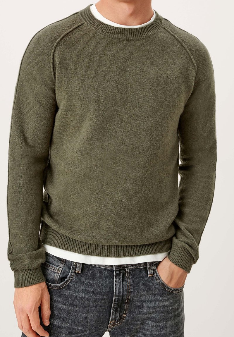 Olivgrüner Pullover mit Rundhalsausschnitt und strukturiertem Strickmuster, mit gerippten Bündchen und Saum, über einem weißen Hemd getragen, kombiniert mit dunklen Jeans.