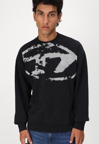 Sort sweatshirt lavet af bomuld med et stort gråt abstrakt design på brystet. Har ribbede ærmer og kant, afslappet pasform.