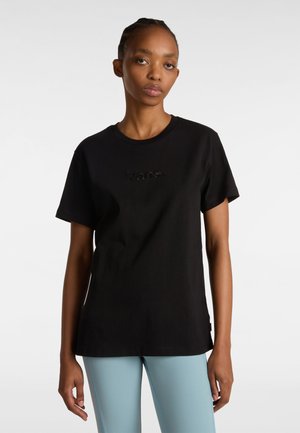 T-shirt noir en coton avec le logo "Vans" brodé sur la poitrine, manches courtes et coupe décontractée. Porté avec des leggings bleu clair.