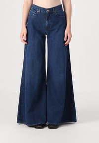 Korkeat vyötäröiset, tummansiniset, väljät farkut, joissa on suuret takataskut ja hieno haalistuma. Klassinen viiden taskun muotoilu hopeaosilla.