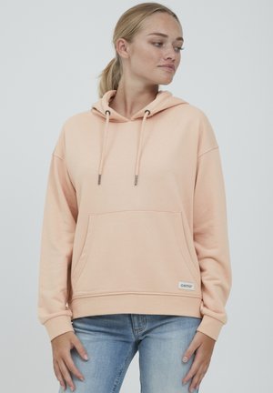 Sudadera de color durazno hecha de tela suave, con un bolsillo frontal, capucha con cordón y puños acanalados. Logotipo de la marca sutil en el dobladillo.