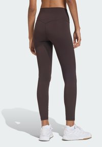 Leggings marroni a vita alta realizzati in materiale elastico, con una texture liscia e un design attillato. Abbinati a scarpe da ginnastica bianche.