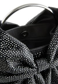 Juoda rankinė su sidabriniais kaiščiais, šilkinio audinio, unikalios lankelio detalės ir apvaliu metaliniu rankena. Viduje yra užsegimas su spaustuku.