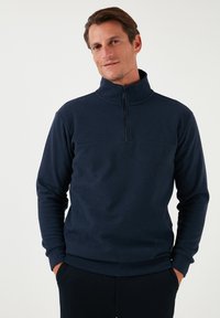 Pullover navy a mezza zip realizzato in morbido tessuto a maglia. Presenta un colletto alto e polsini e orlo a coste. Design semplice e pulito senza motivi.