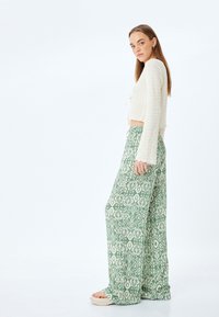 Gehaakte crème top met lange mouwen, gecombineerd met groene wijde broek met een geometrisch patroon. Gladde textuur, ontspannen pasvorm.