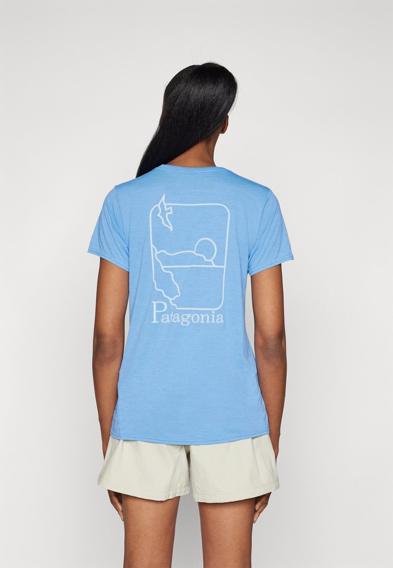 Lysblå t-shirt med en hvid omridsgrafik, der viser abstrakte former og ordet "Patagonia" nederst, korte ærmer.