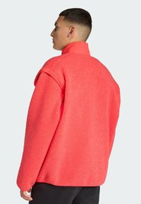 Chaqueta de forro polar color coral con cuello alto, corte holgado y superficie texturizada. Presenta mangas cortas y un dobladillo limpio.