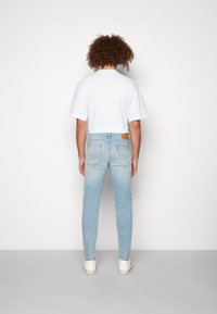 Vitt kort t-shirt i kombination med ljusblå skinny jeans. Anmärkningsvärda detaljer är en brun läderlapp på baksidan av jeansen.