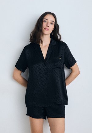 Ensemble en satin noir à manches courtes comprenant une chemise et un short, arborant un motif subtil, un col en V, une poche poitrine et un petit logo de marque.