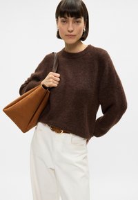 Καφέ πλεκτό πουλόβερ με στρογγυλή λαιμόκοψη, συνδυασμένο με ψηλόμεσα λευκά παντελόνια και καφέ τσάντα ώμου, με λείες υφές και μινιμαλιστικό σχέδιο.