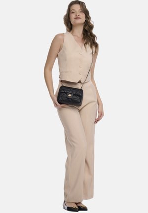 Beige gestreepte vest en bijpassende broeken. Model draagt een zwarte gewatteerde handtas met een gouden sluiting. Zwarte schoenen met decoratieve accenten.