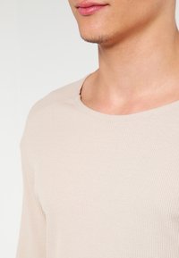 Ljus beige långärmad ribbad tröja med rund halsringning och texturerad tygkvalitet. Den figursydda designen ger en bekväm passform.