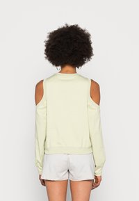 Kalte-Schulter-Sweatshirt in Hellgrün, mit gerippten Bündchen und Saum, weicher Textur und lässiger Passform. Getragen mit hellgrauen Shorts.