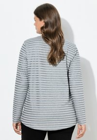 Langärmliges graues Shirt mit blauen horizontalen Streifen, aus weichem Stoff gefertigt. Verfügt über einen abgerundeten Saum und einen lockeren Schnitt.