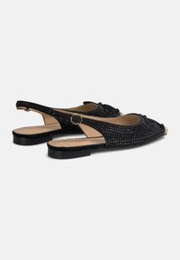 Schwarze Slingback-Schuhe mit durchbrochenem Design. Sie verfügen über eine flache Sohle, eine runde Zehenpartie und eine Schleifendetail an der Vorderseite. Goldene Akzente an der Zehenpartie.