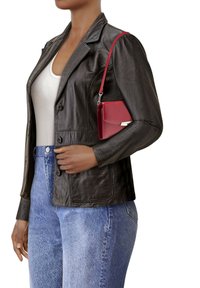 Giacca di pelle nera con un design aderente, abbinata a jeans in denim azzurro. Una piccola borsa rossa con tracolla è indossata sulla spalla.