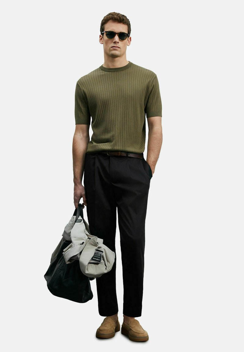 Olivgrünes geripptes kurzärmliges Stricktop, schwarze maßgeschneiderte Hose, braune Wildleder-Lederslipper und eine große beige-schwarze Schultertasche.