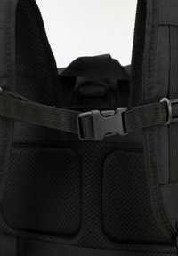 Mochila de tela negra con parte superior y correas ajustables, que presenta un cierre de plástico y un acolchado de malla para mayor comodidad. Superficie texturizada con costuras visibles.