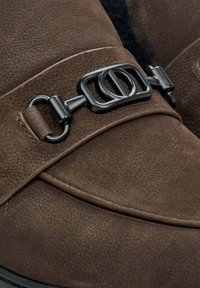 Brown leather shoes featuring a smooth texture, with a decorative black metal buckle and strap across the upper.
